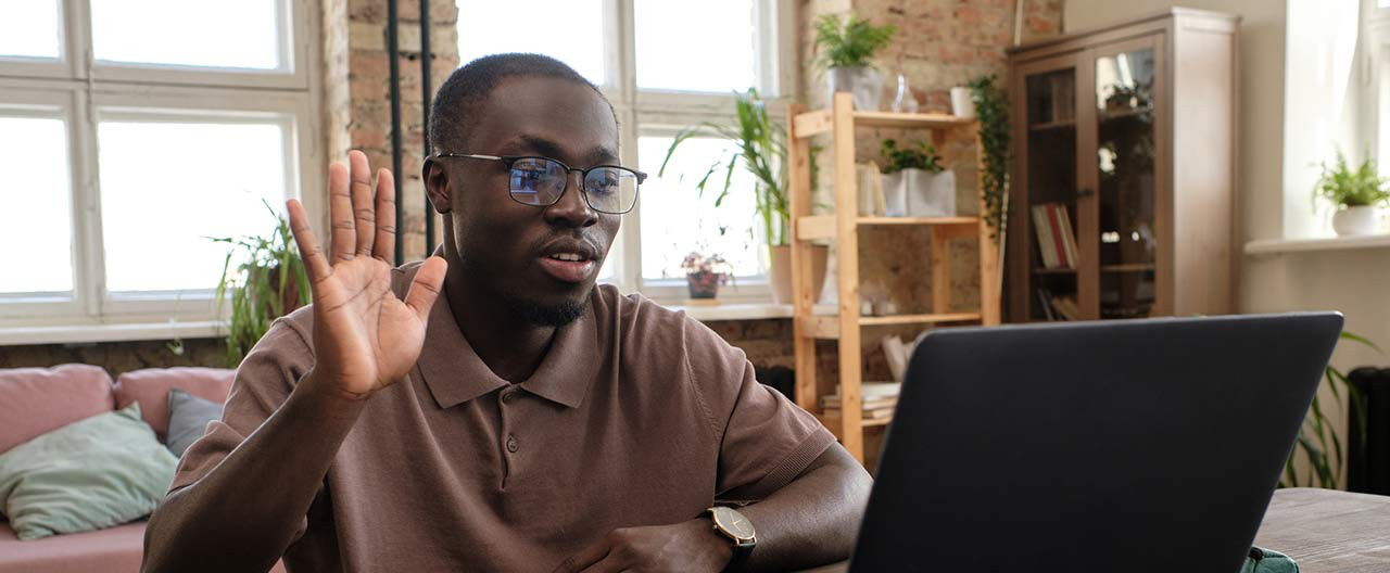 man working from home waving to laptop