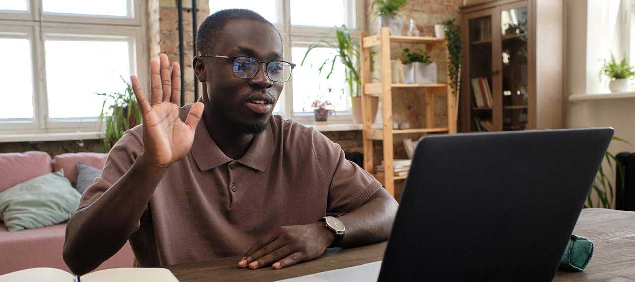 man working from home waving on zoom